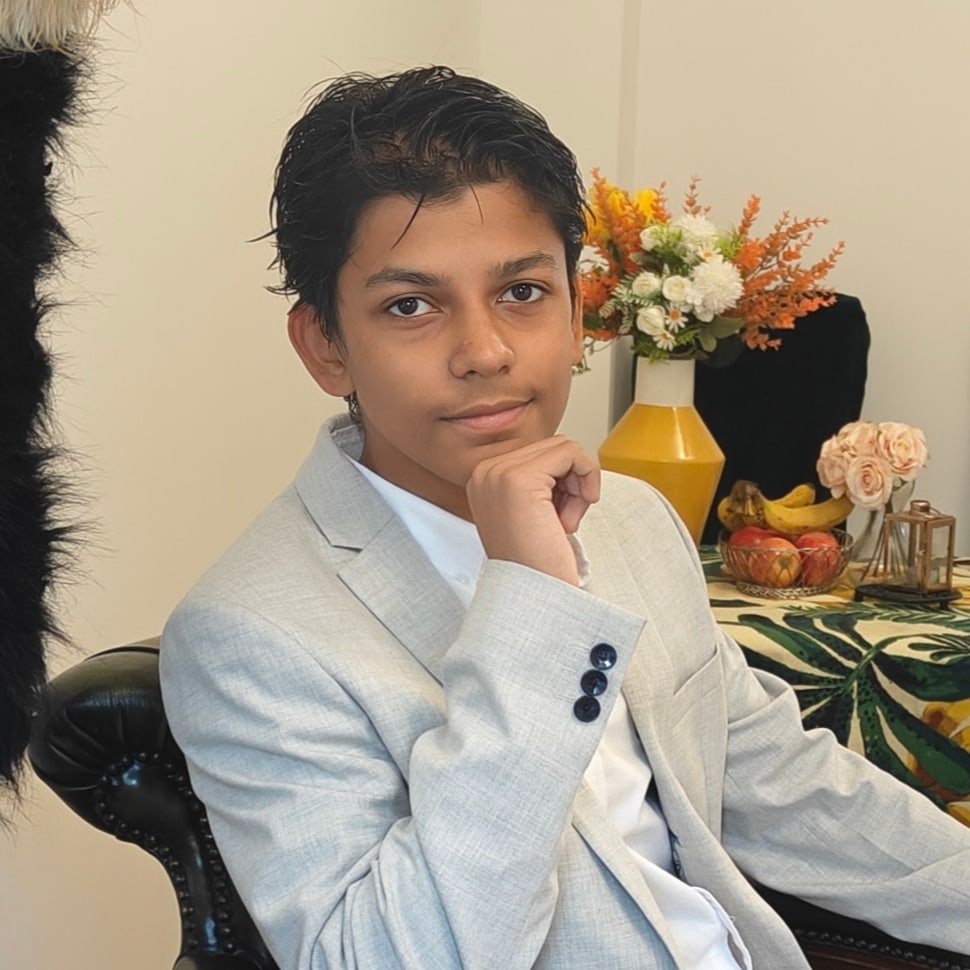 Aarush seated at a table in his suit, with his full face visible