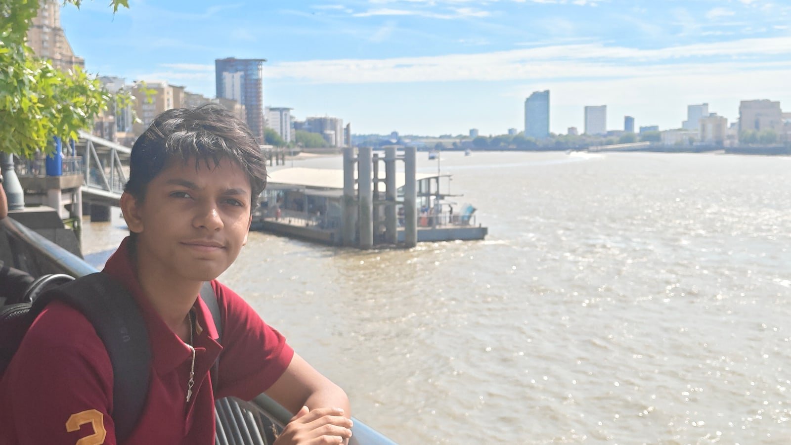 Aarush in a maroon polo beside the river, with the waterfront behind him